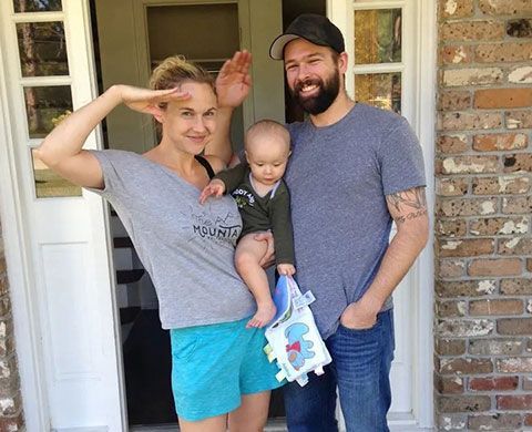 A man and woman holding a baby in front of a brick building