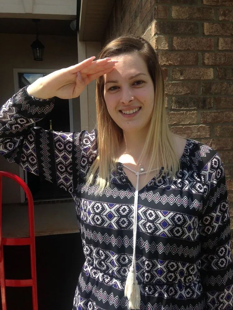 A woman is saluting in front of a brick building.