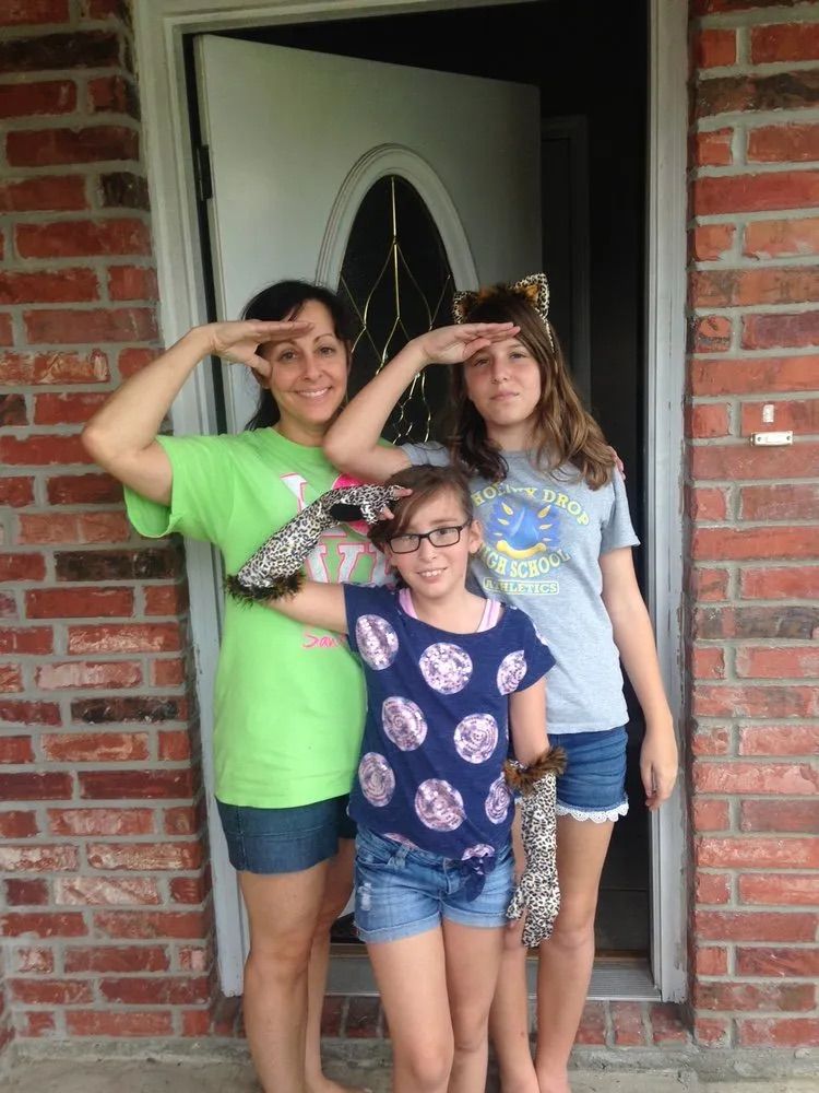 Three girls are posing for a picture in front of a brick house.