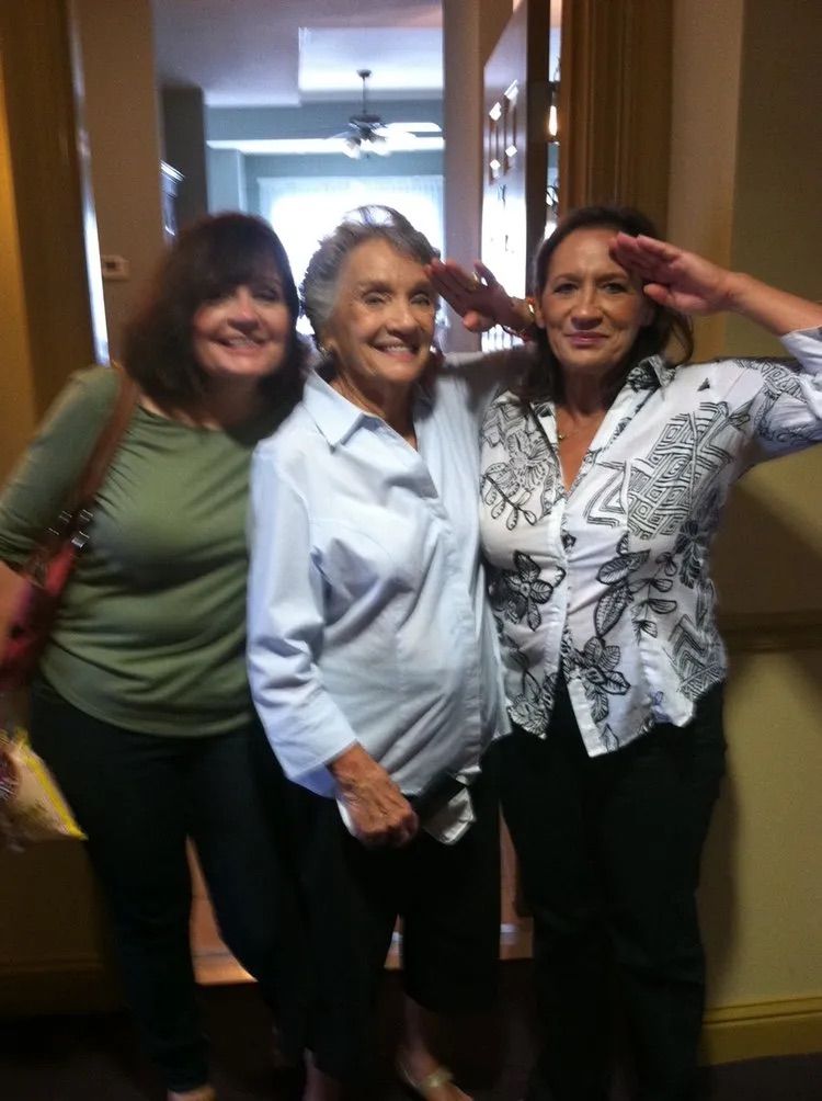Three women are posing for a picture and one is saluting
