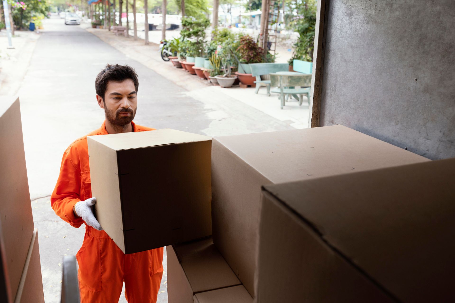 A man in an orange jumpsuit is carrying a cardboard box.