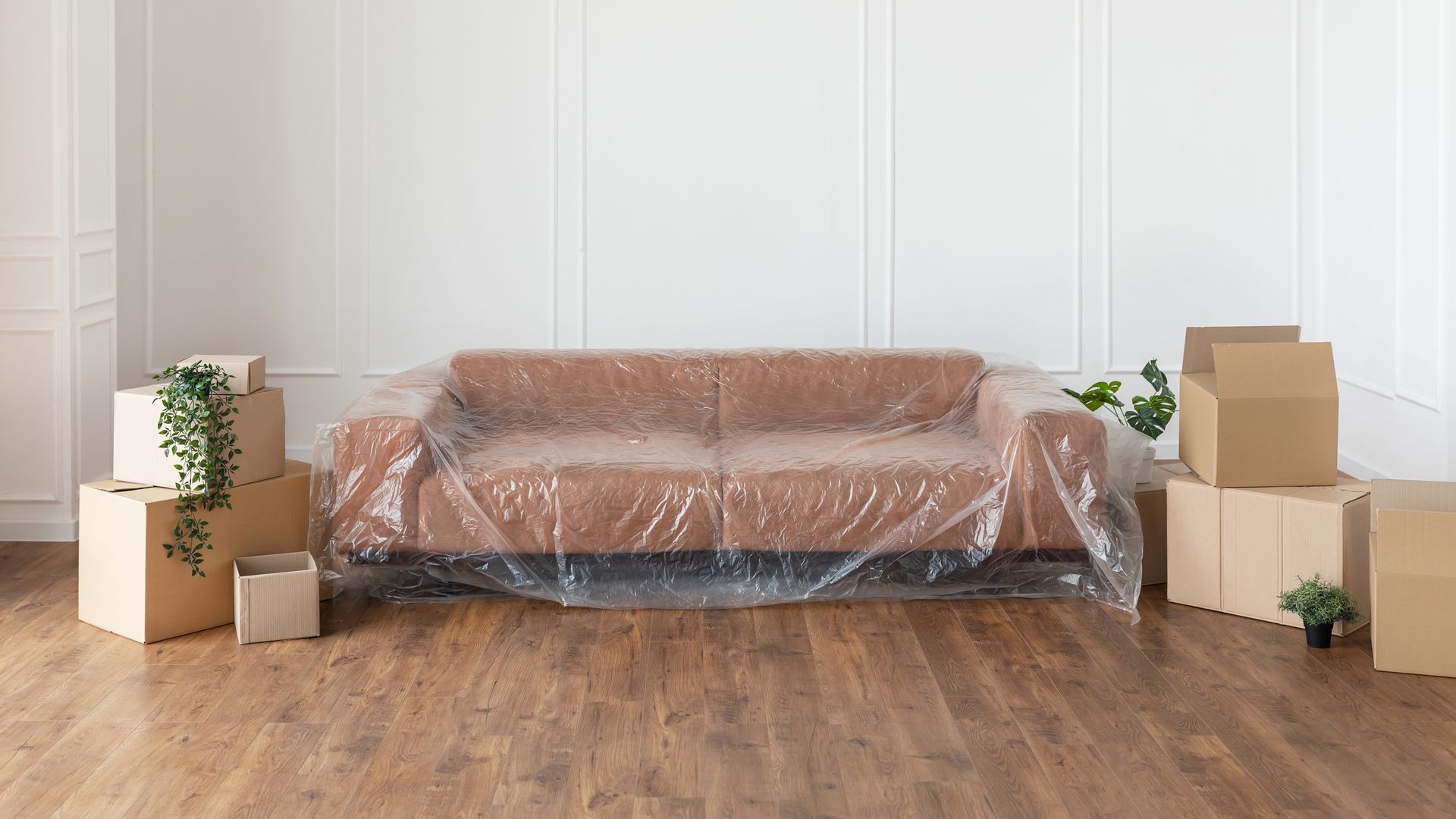 A living room with a couch wrapped in plastic and cardboard boxes.