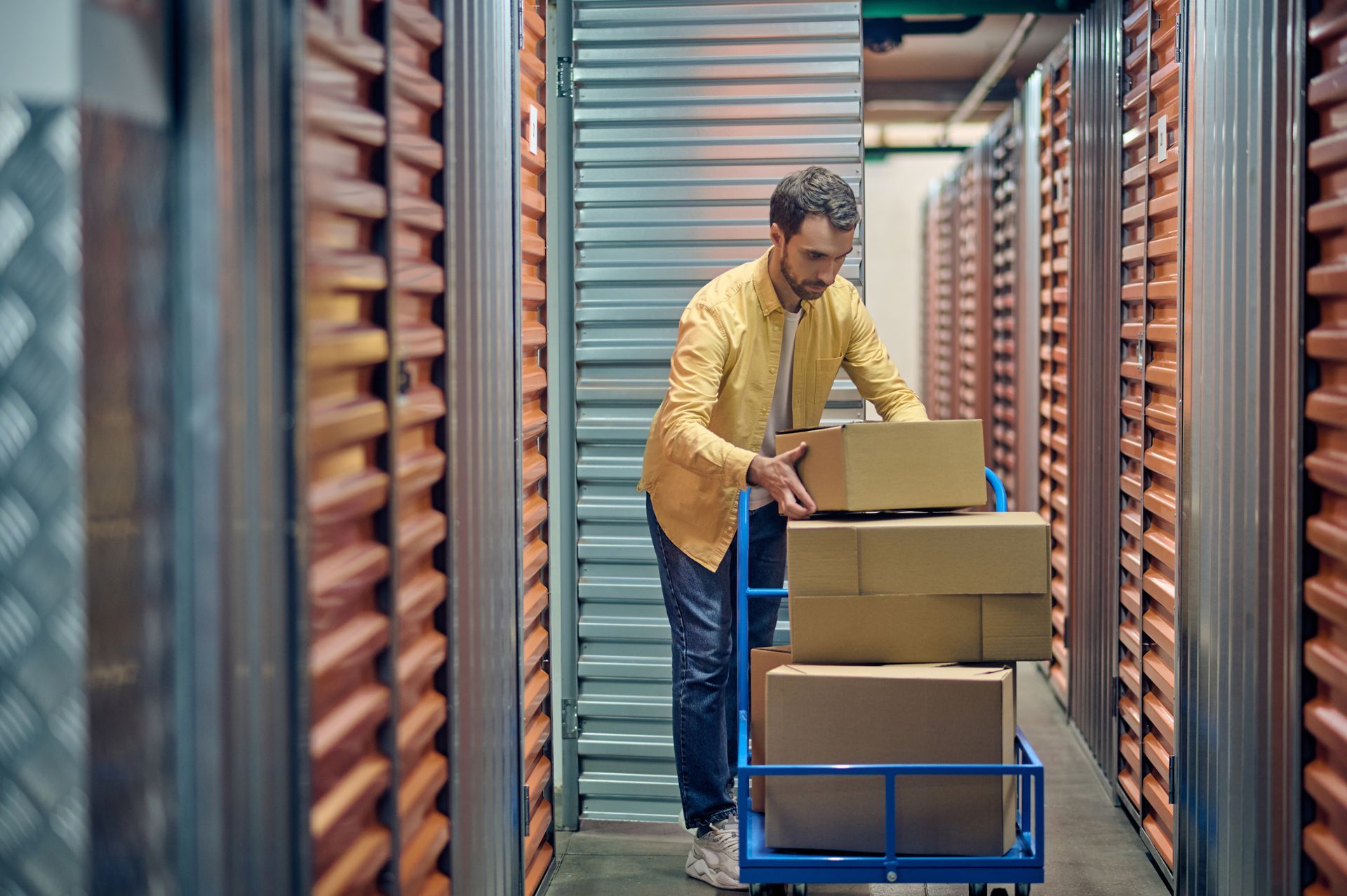 A man is pushing a cart filled with boxes in a storage room.