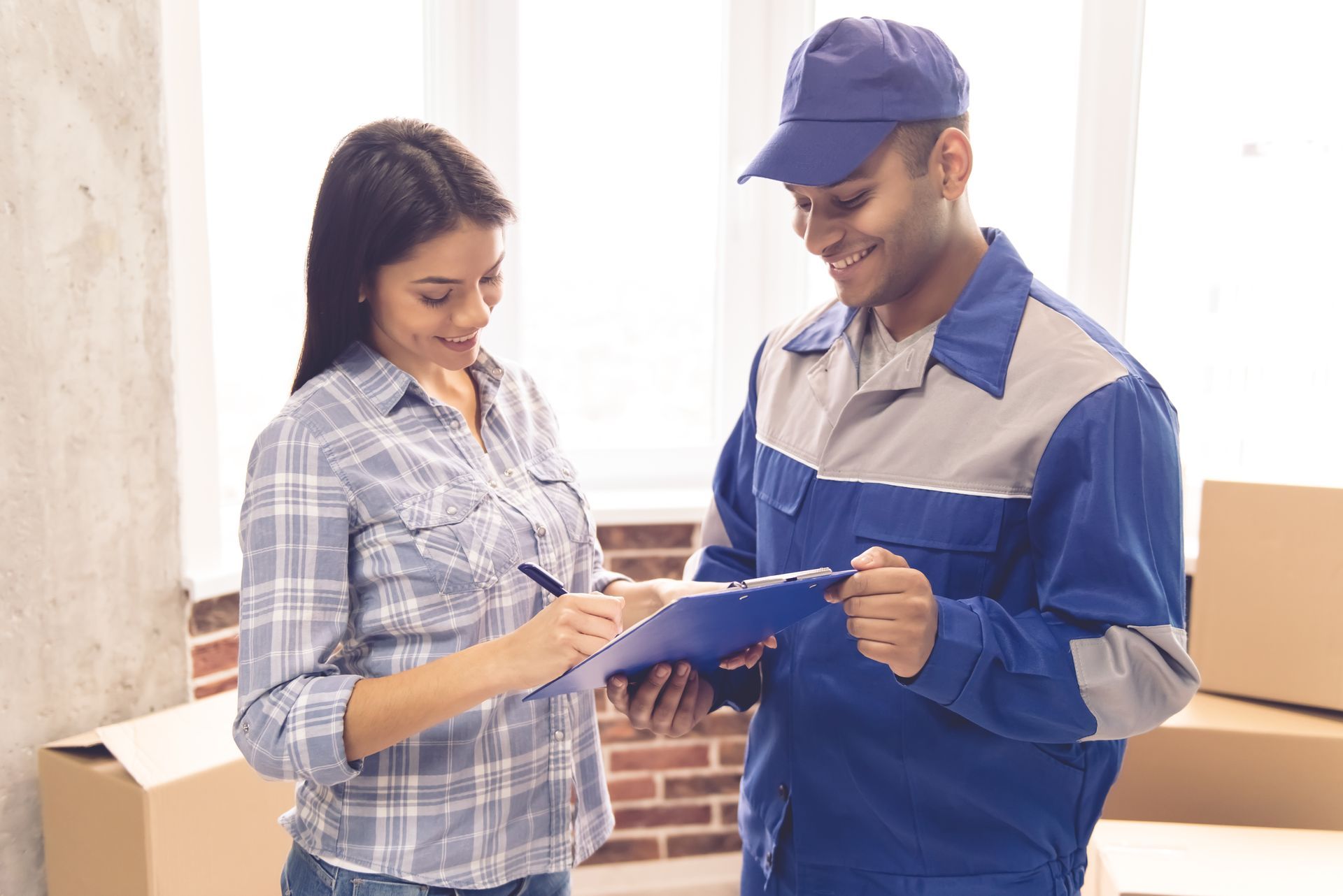 A delivery man is talking to a woman while holding a clipboard.
