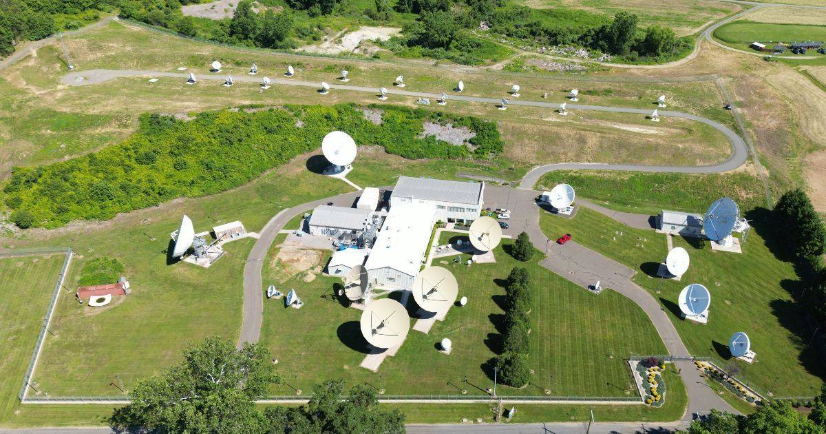 Image shows COMSAT's Southbury Teleport in Connecticut, USA. On a green lawn, dozens of satellite communication antennas of varying sizes are seen, surrounding a central building complex