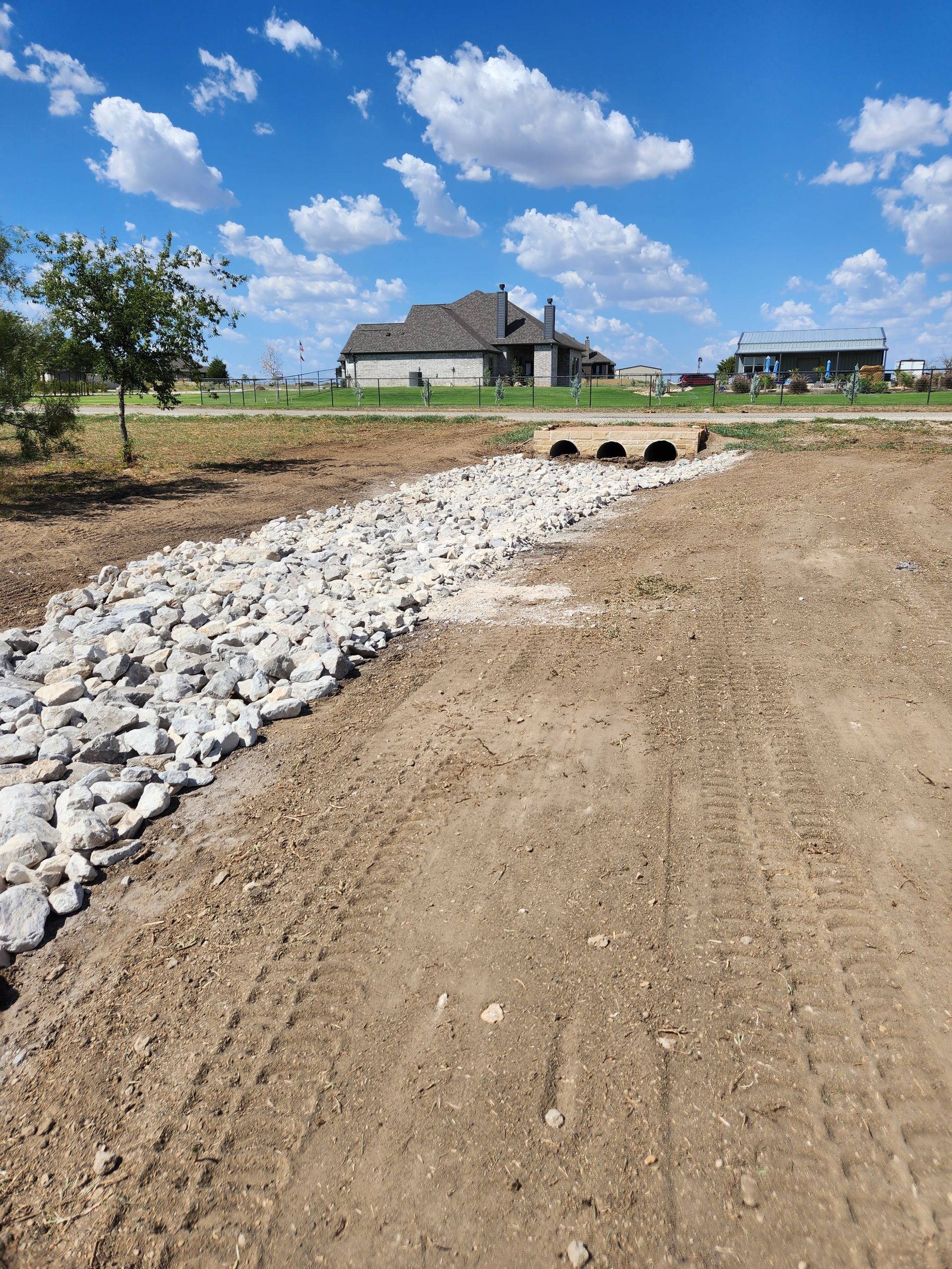 A dirt road going through a field with a house in the background.