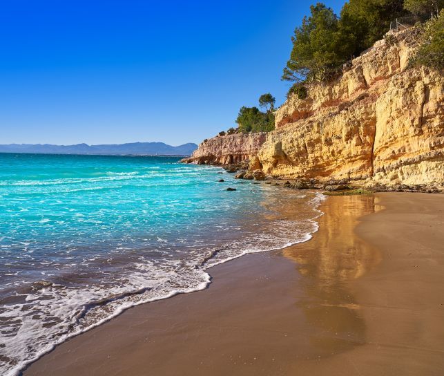 Una playa con un acantilado al fondo y un océano turquesa.