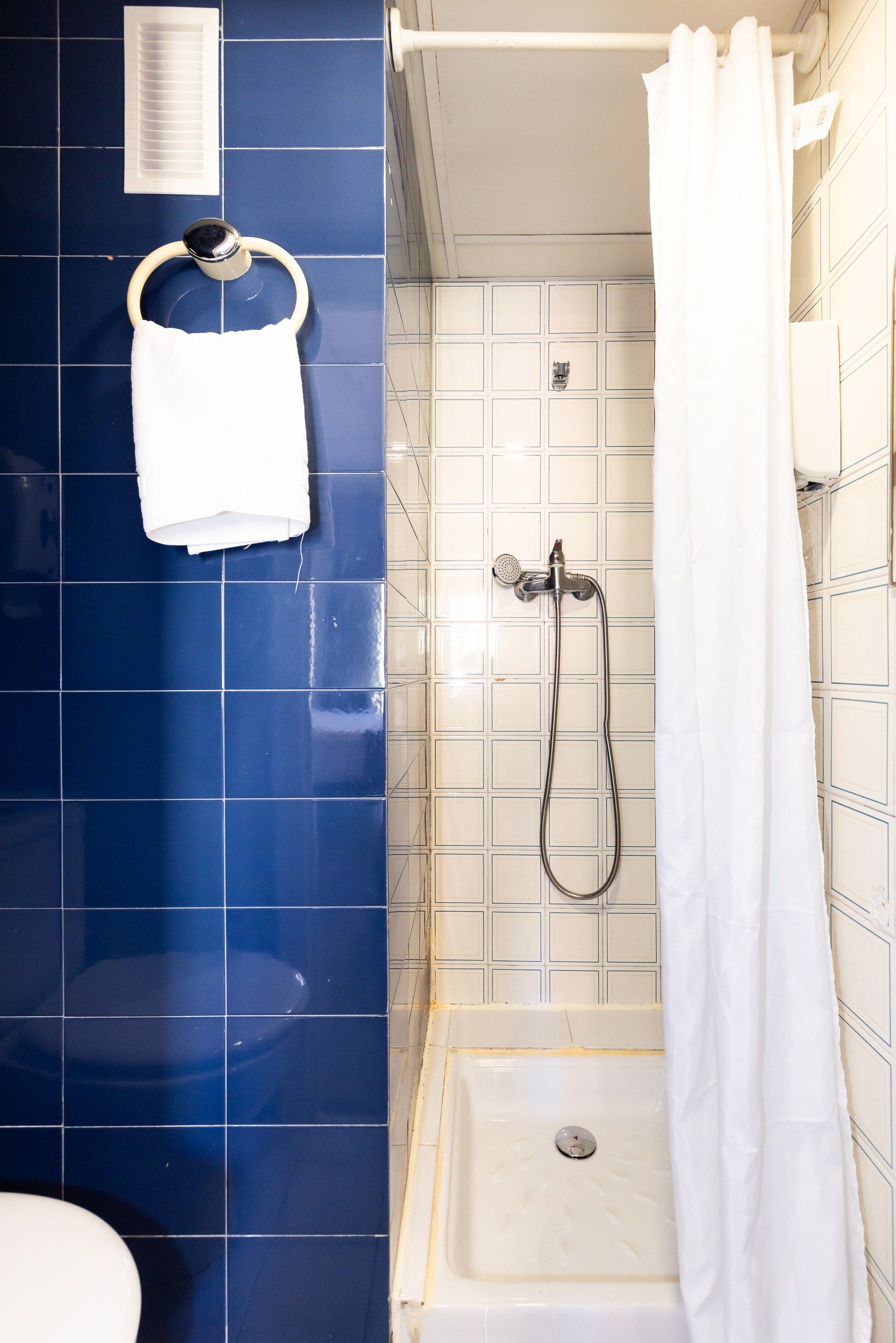 Un baño con azulejos azules y una cortina de ducha blanca.