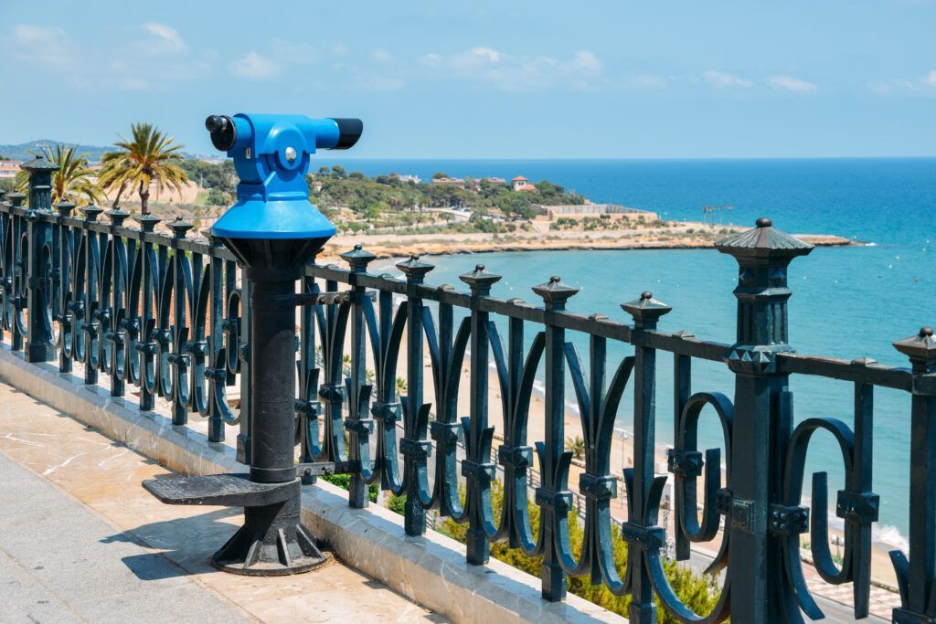 Unos binoculares azules están junto a una valla con vistas al océano.