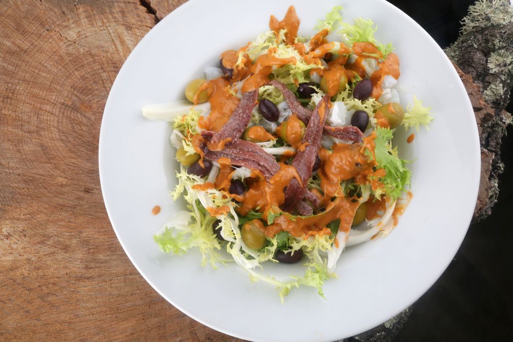 Un plato blanco cubierto con ensalada sobre una mesa de madera.