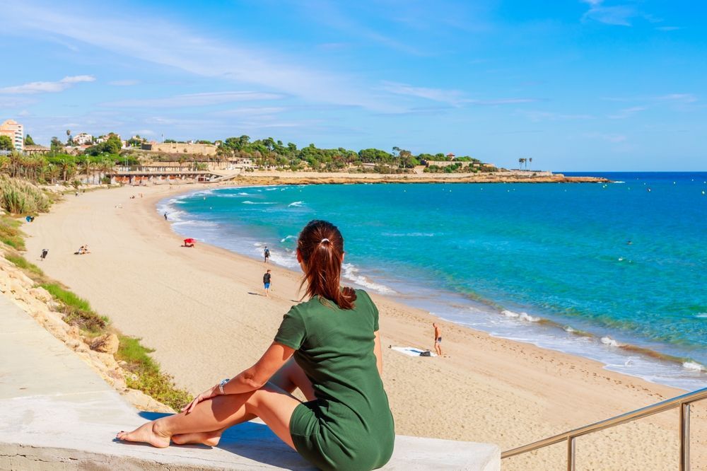 Una mujer está sentada en una cornisa con vistas a una playa.