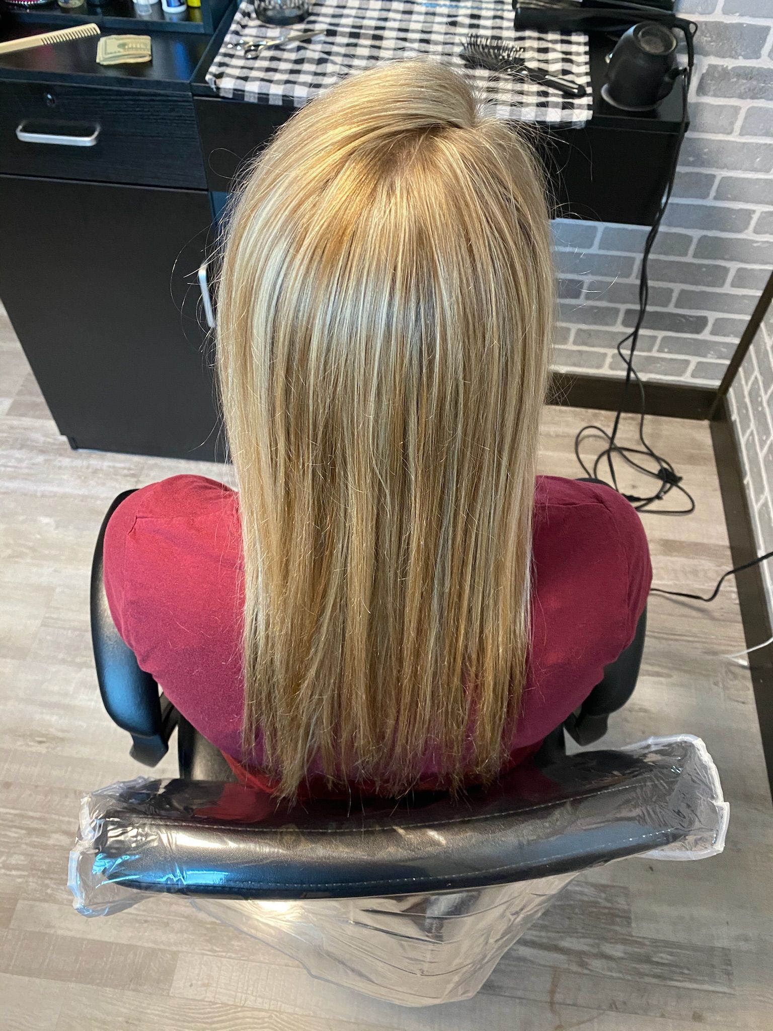 Blond hair styled, straight and long, on a person in a salon chair, red top.