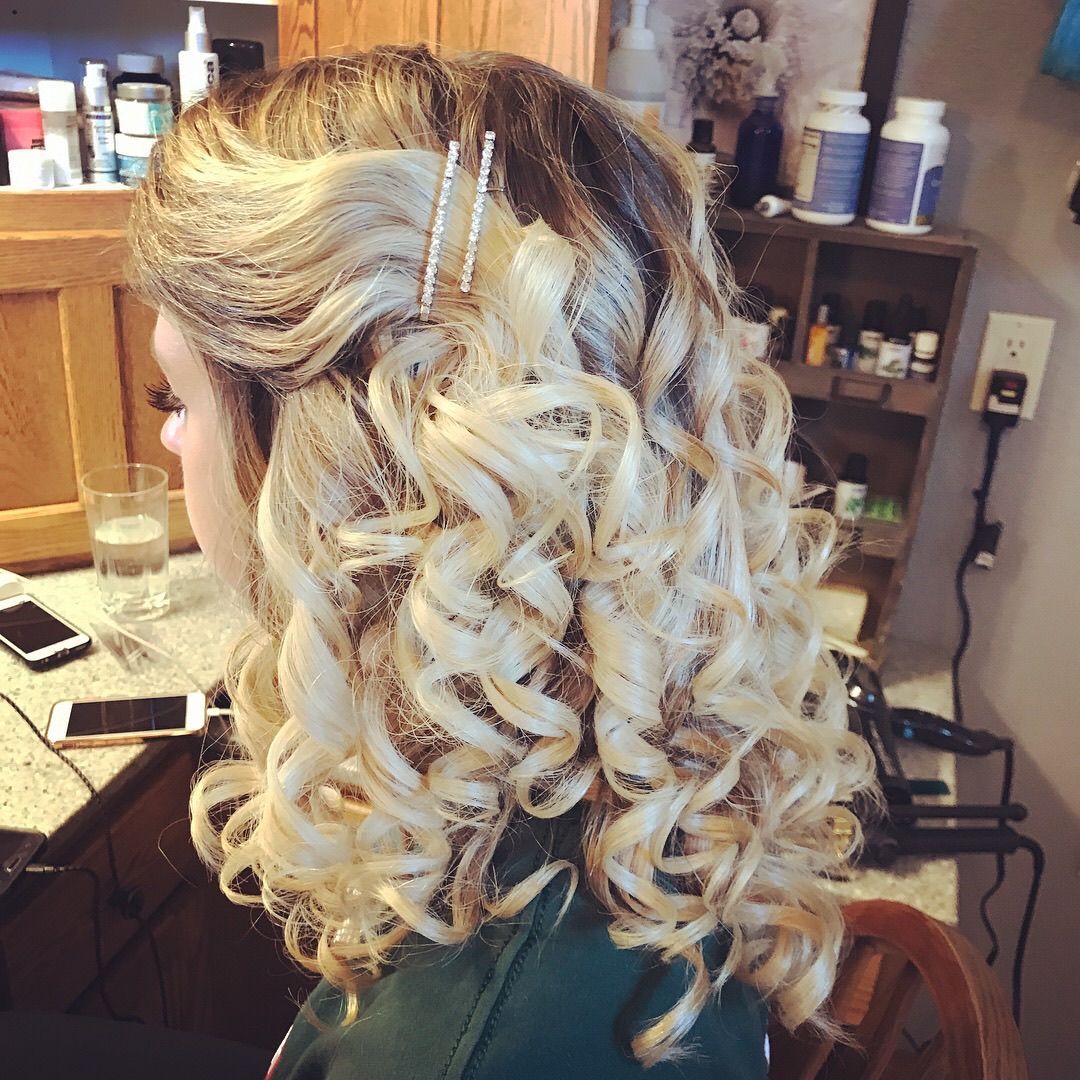 Woman with blonde, curly hair styled half up, adorned with jeweled pins.
