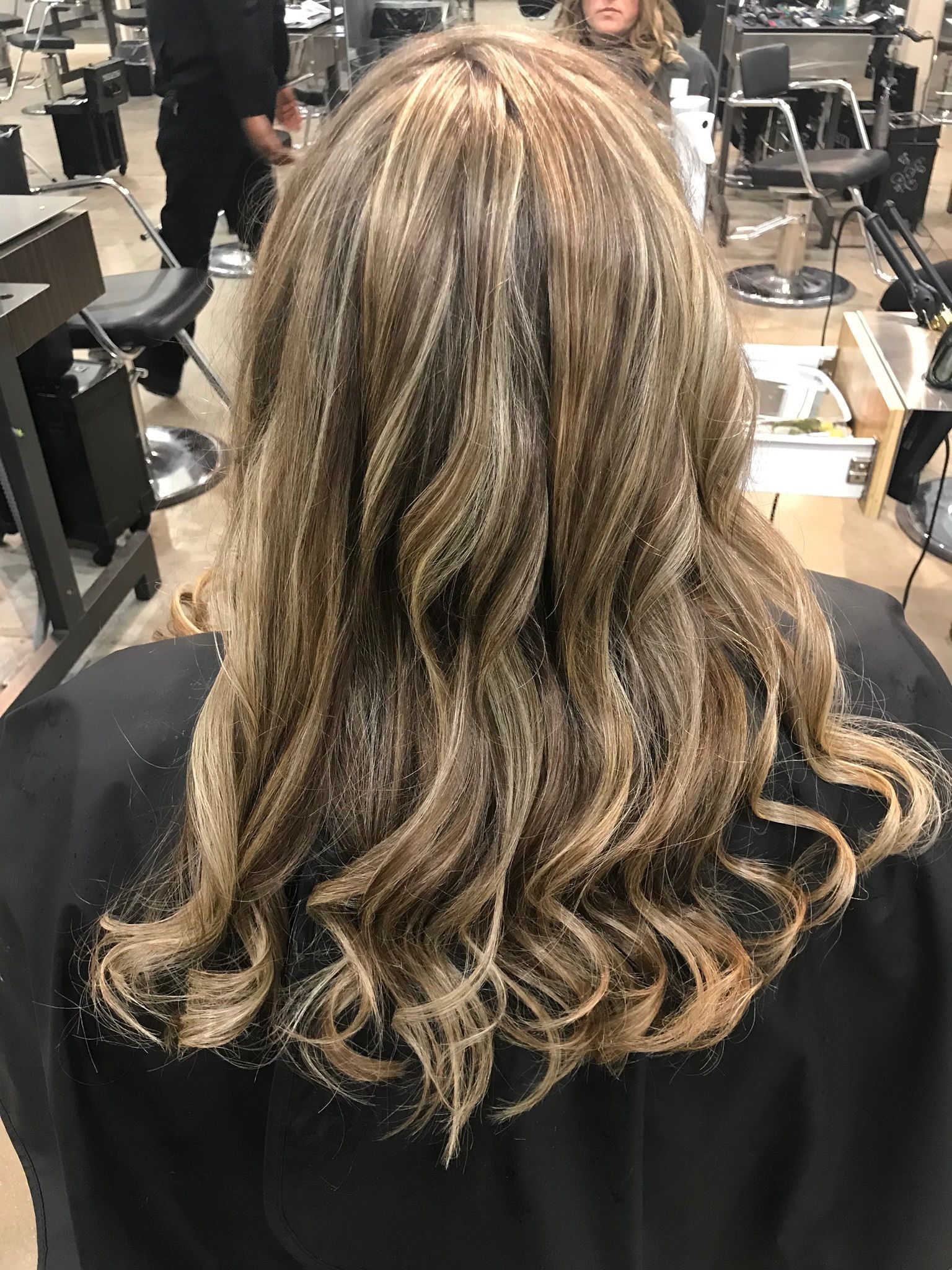 Woman with wavy brown and blonde highlighted hair in a salon chair.