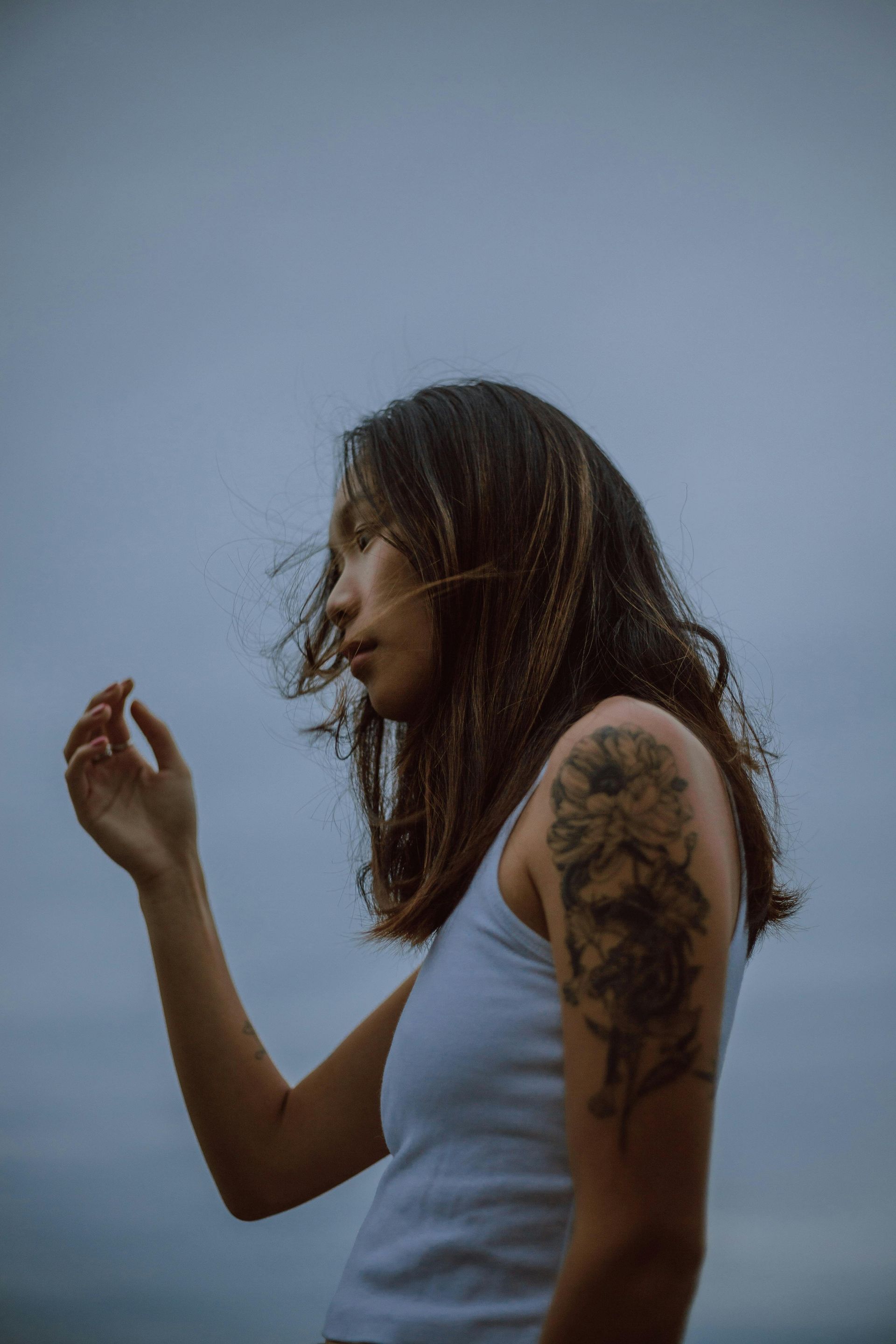 A woman with a tattoo on her arm is standing in front of a cloudy sky.