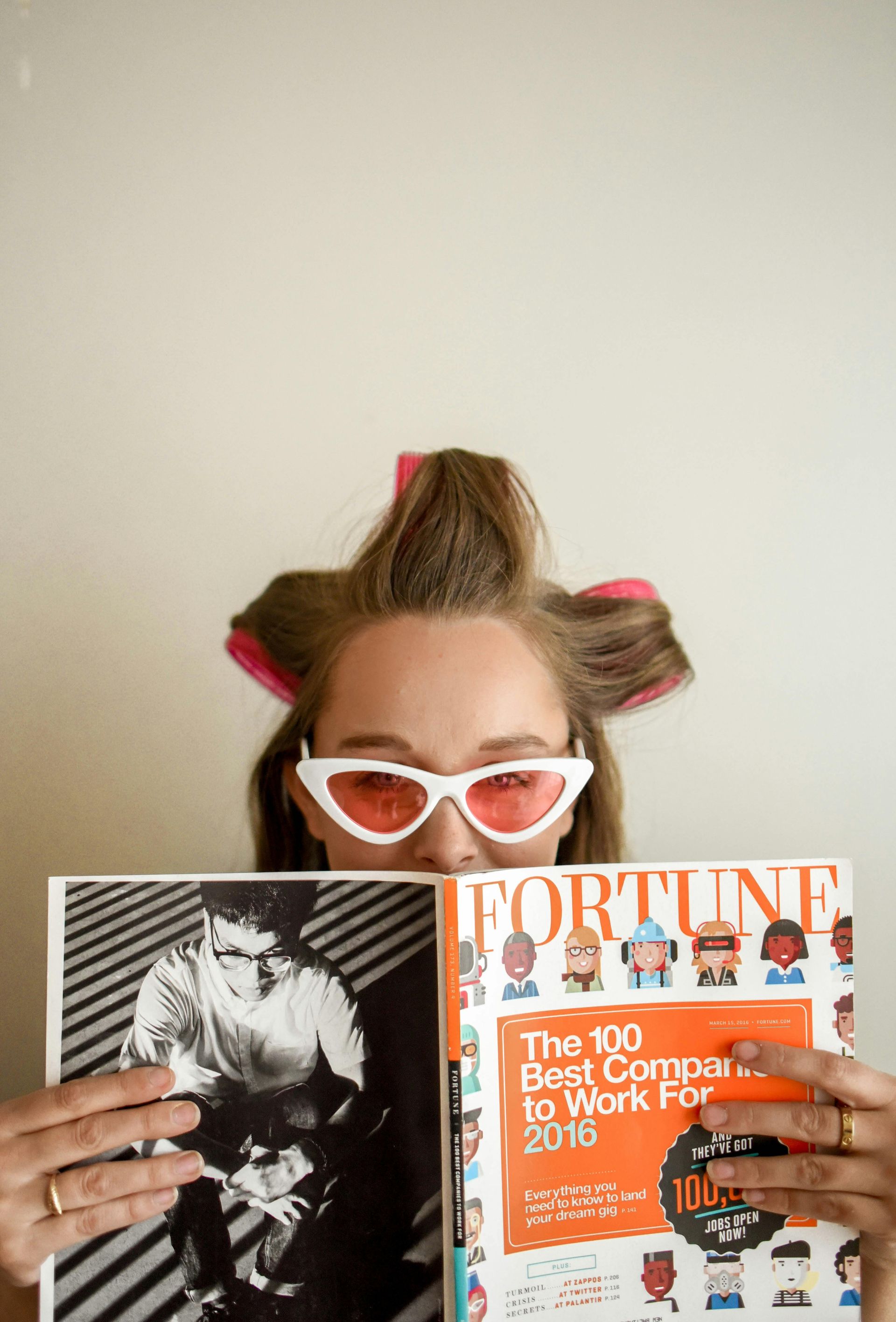 A woman with curlers in her hair is holding a magazine.