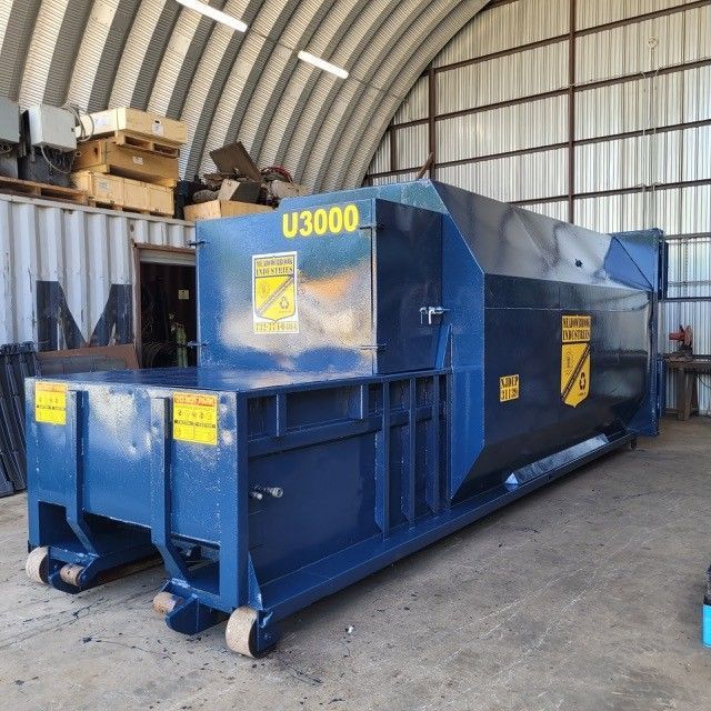 A large blue industrial trash compactor, marked 