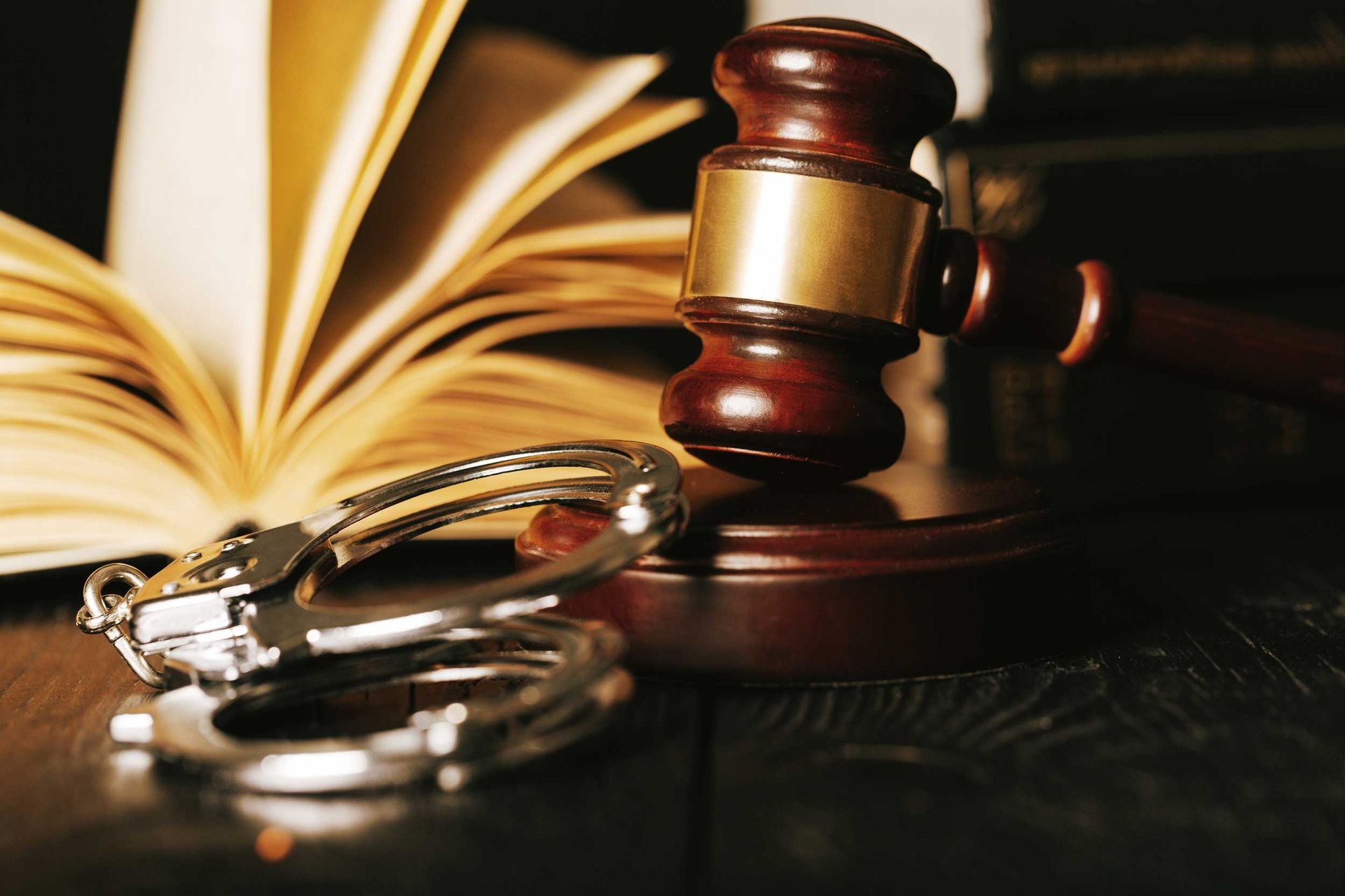 Gavel, handcuffs, and open law book on a dark wooden surface.