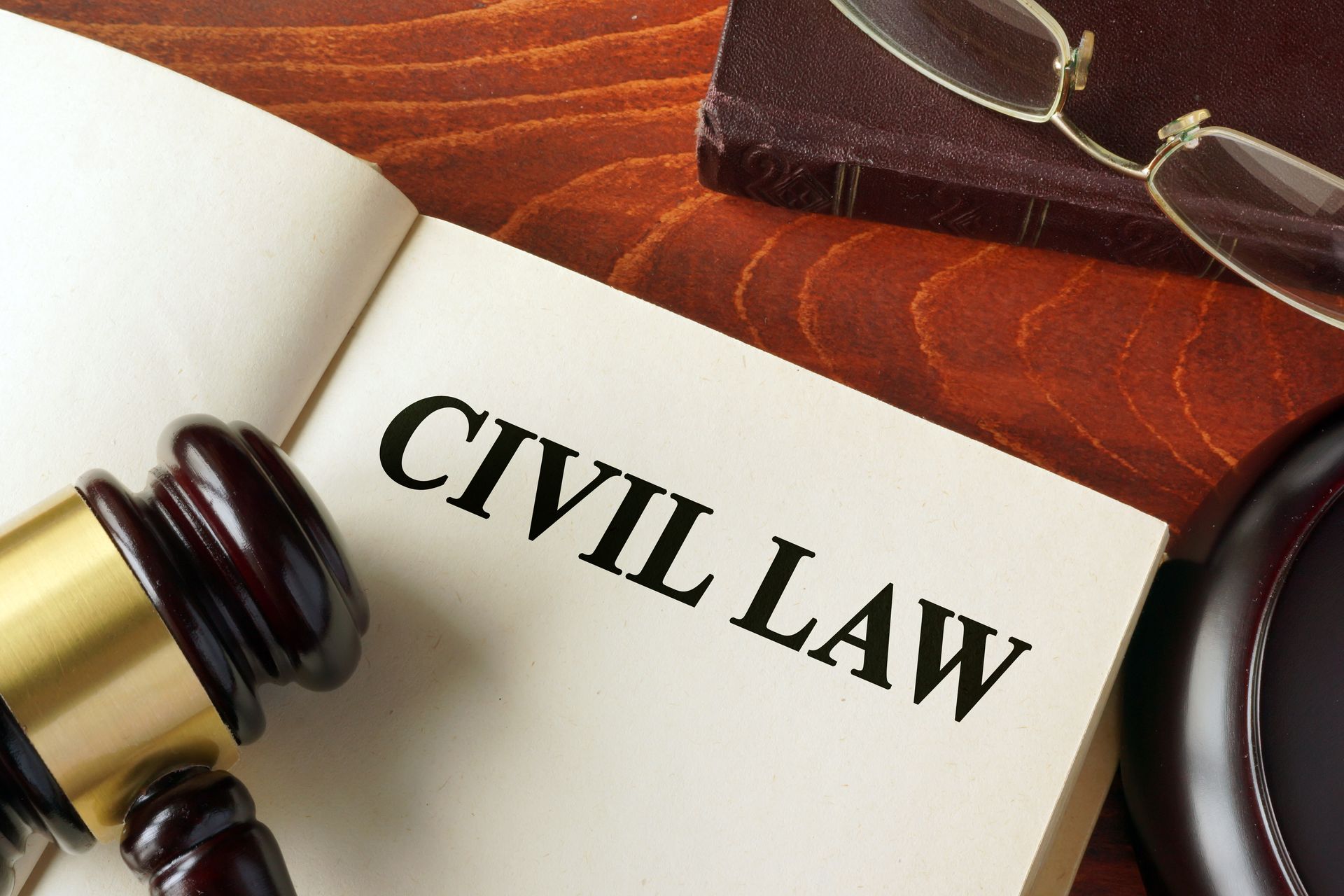 A law book opened to the words “Civil Law” rests beside a gavel and reading glasses on a desk.