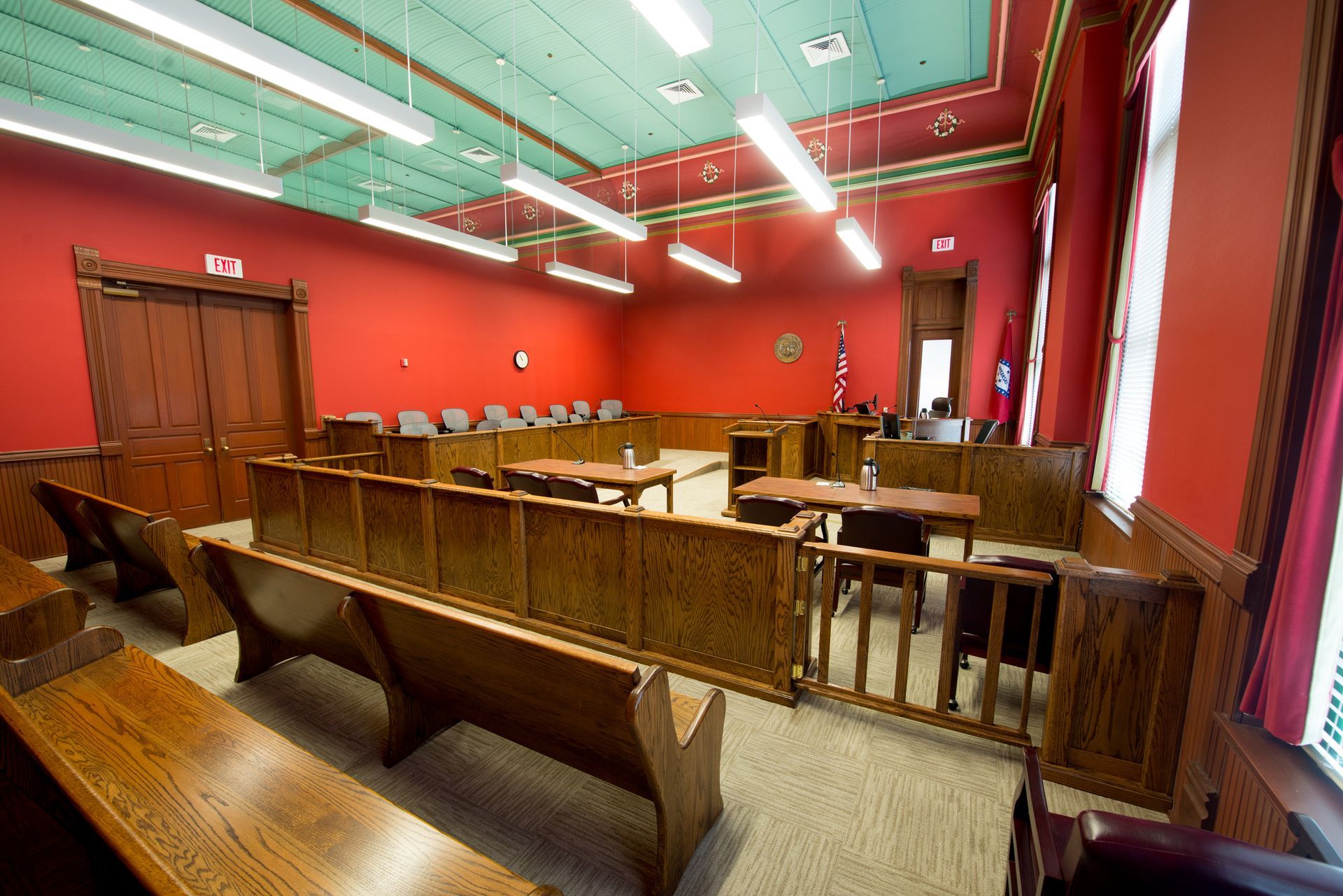 Courtroom interior: red walls, wooden benches and furniture, empty jury box, judge's bench in the background.
