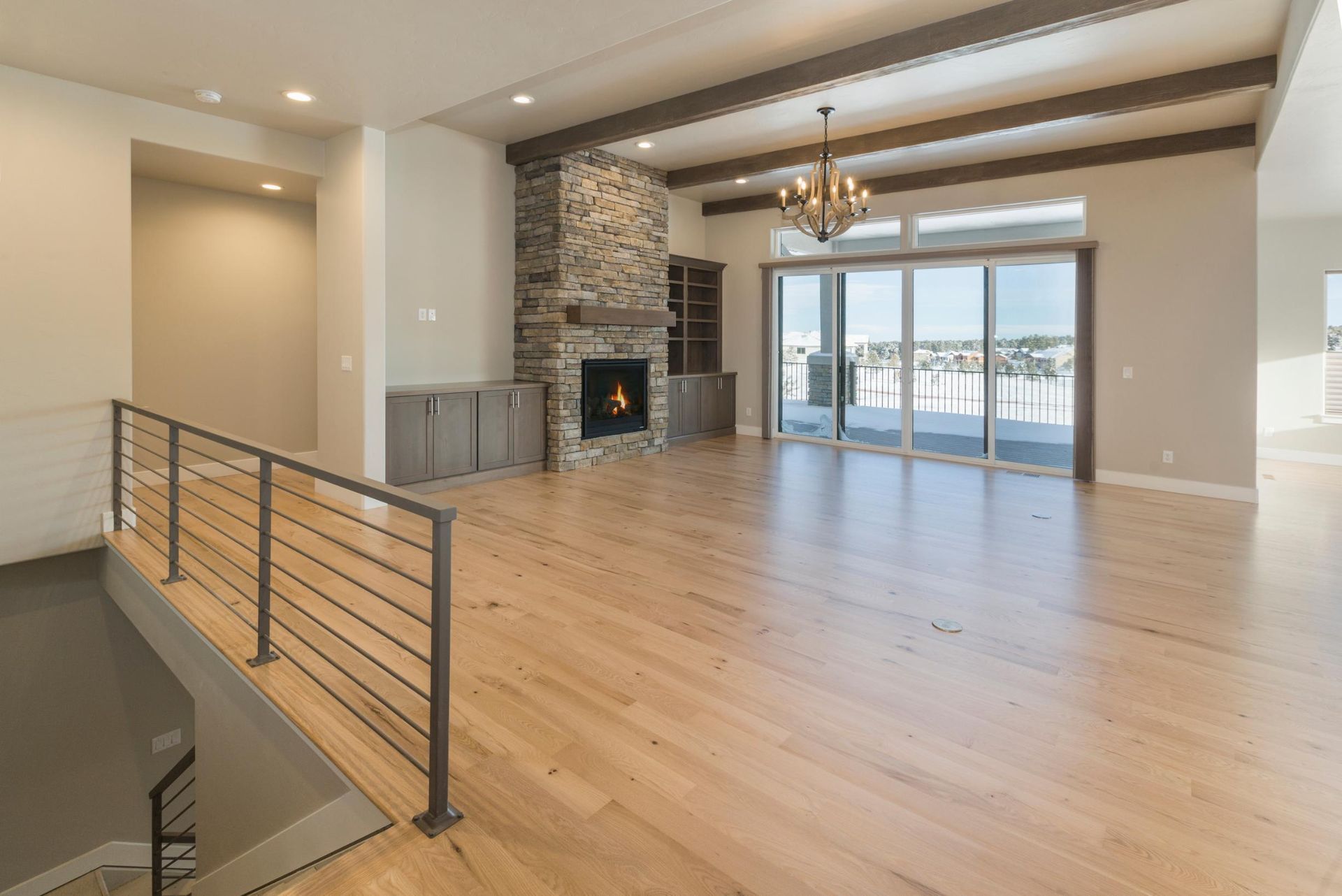 A modern, open-concept living room with light wood floors, a stone fireplace, and a railing overlooking a staircase.