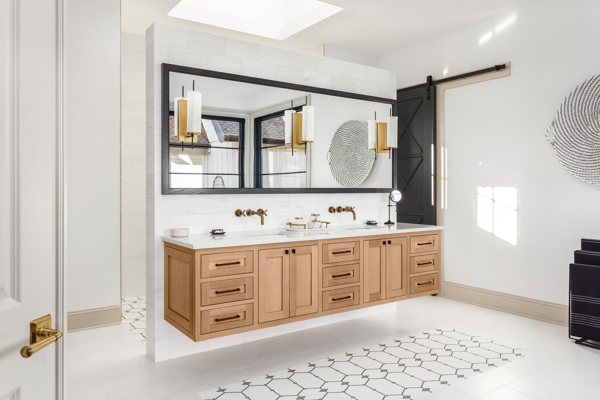 A modern bathroom featuring a floating wooden double vanity, large mirror, and black sliding barn door against white tiles.
