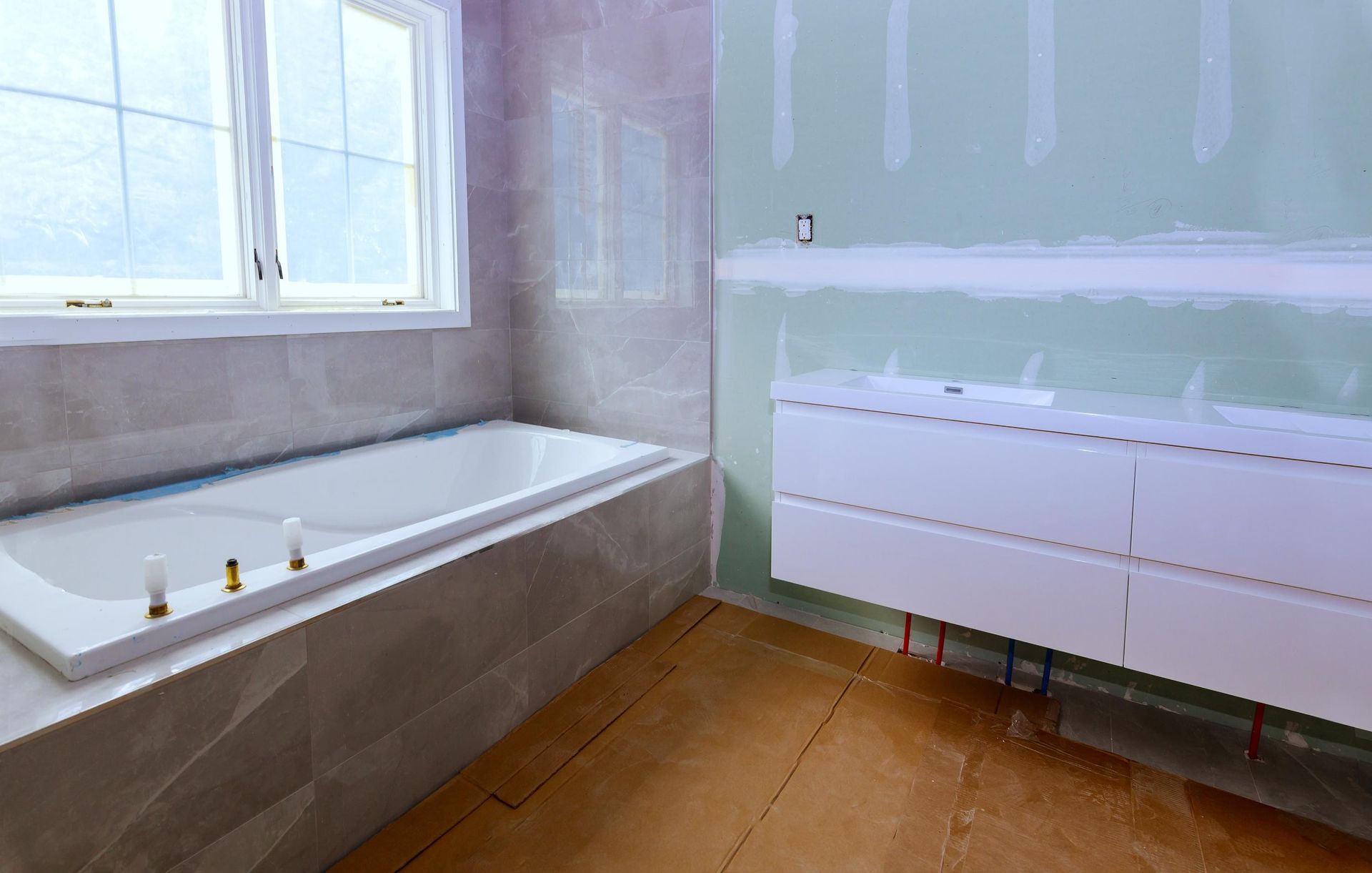 A bathroom under construction with a tiled bathtub, a floating vanity with two sinks, and unfinished drywall walls.