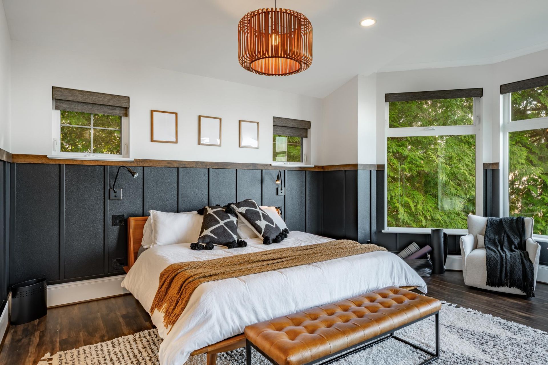 A modern bedroom featuring a bed with white bedding, black patterned pillows, and a tan leather bench in front.