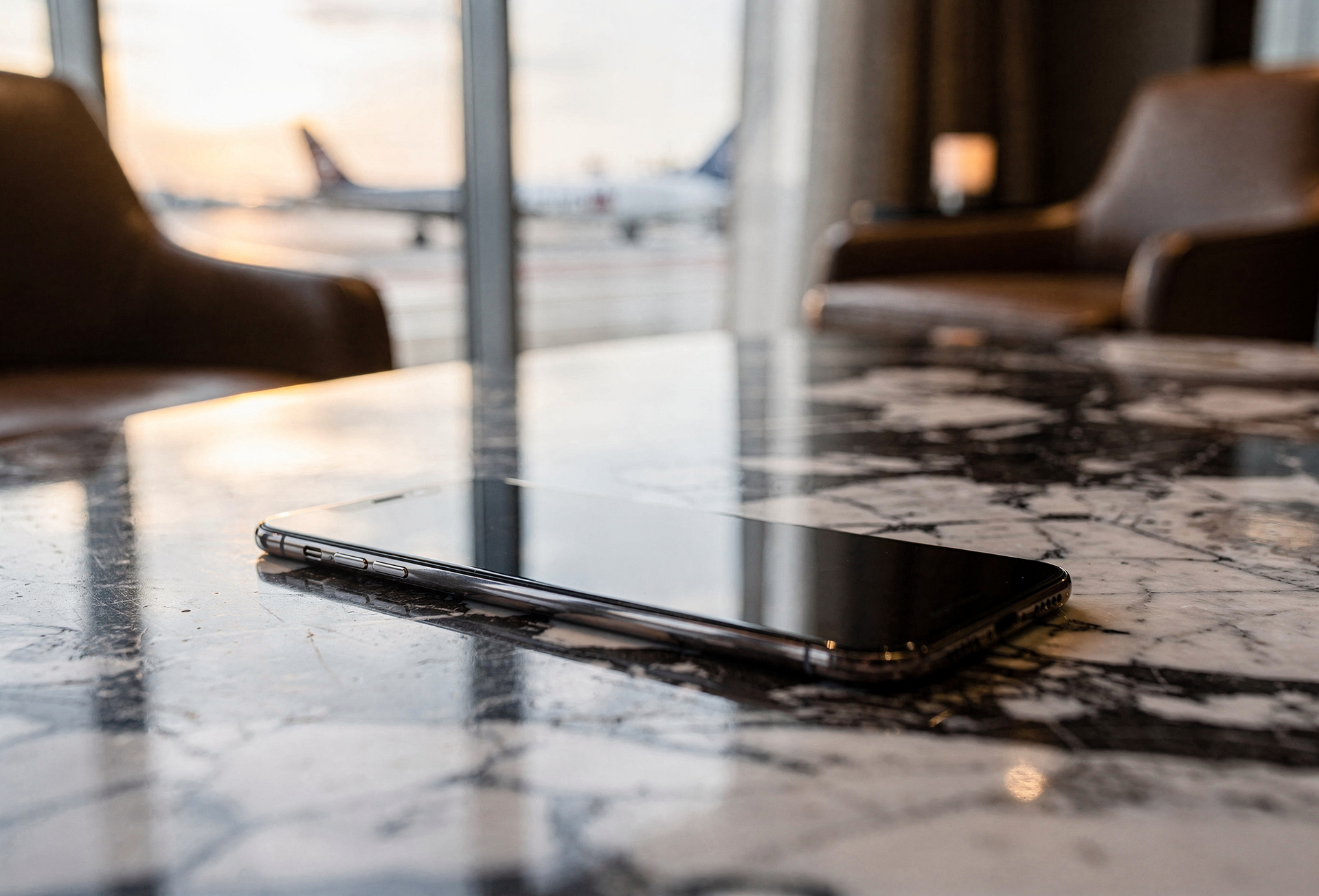 Black smartphone lying on a glossy marble table in a softly lit café or restaurant.