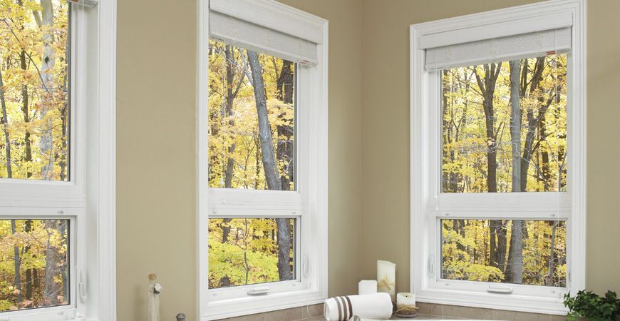 A bathroom with two windows and a sink with a view of the woods.