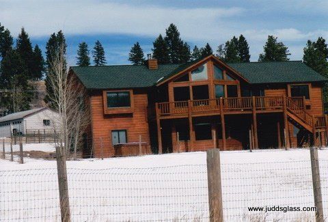 A large log cabin with a green roof is surrounded by snow