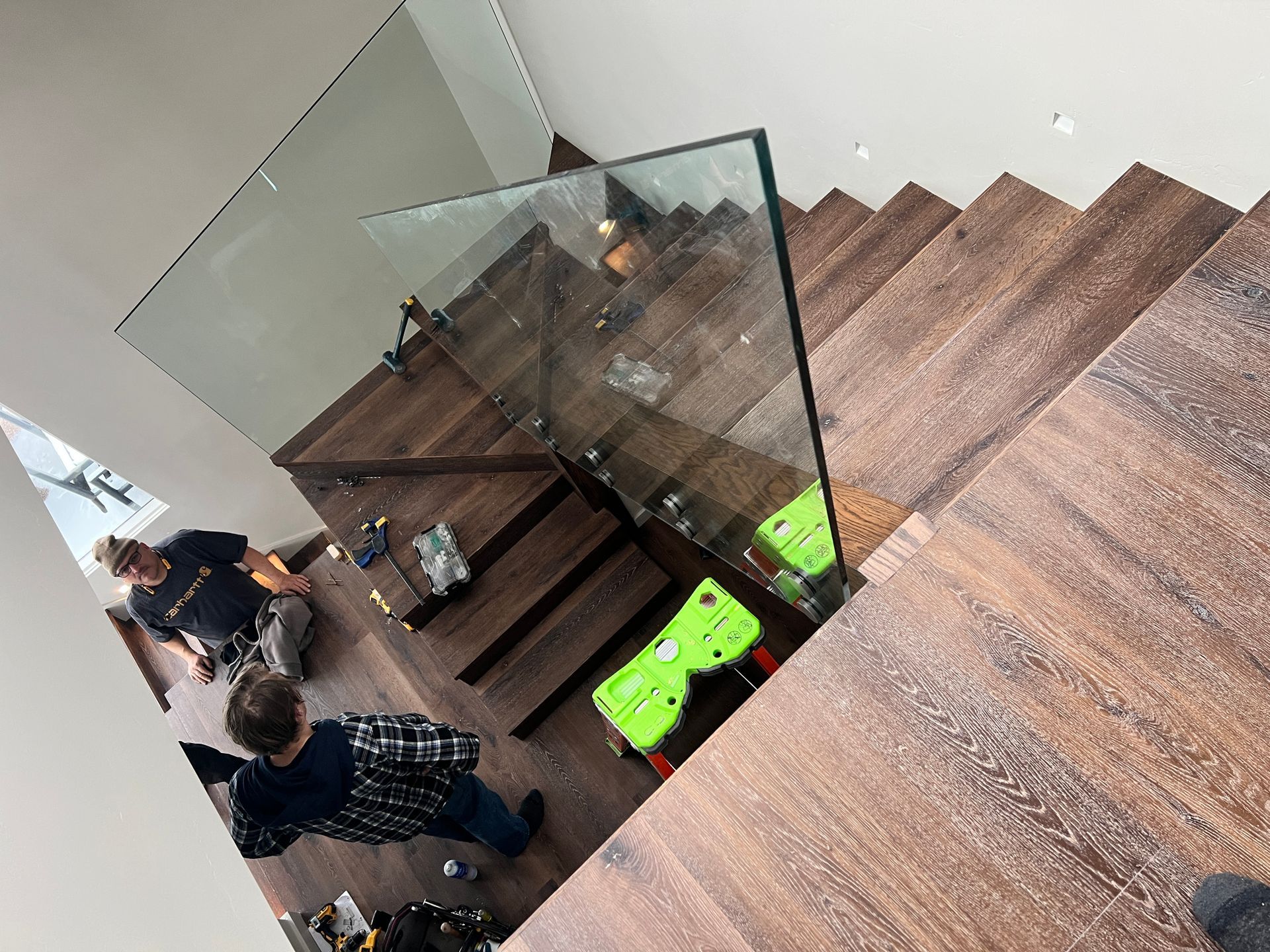 A man is standing on a wooden staircase with a glass railing.