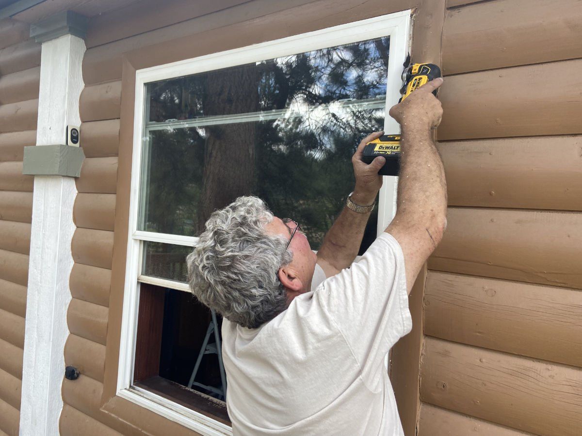 A man is measuring a window on a log cabin with a tape measure.