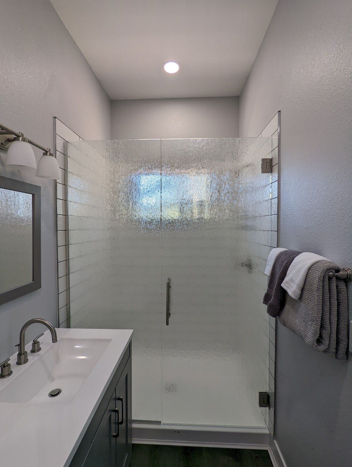 A bathroom with a walk in shower , sink and mirror.