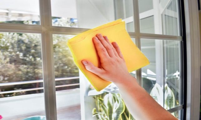 A person is cleaning a window with a yellow cloth.