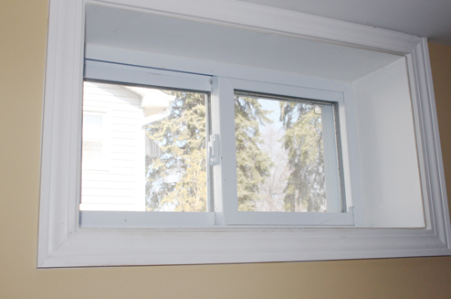A white window with a view of trees in a room.
