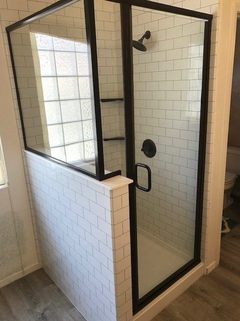 A shower stall with a black frame and white tiles in a bathroom.