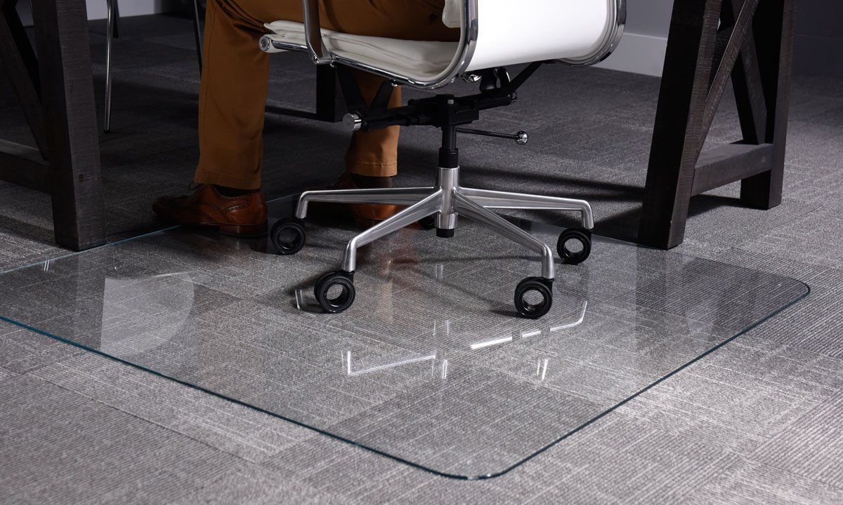 A person is sitting at a desk with a chair on a glass mat.