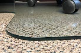 A chair with wheels is sitting on a carpeted floor next to a glass mat.