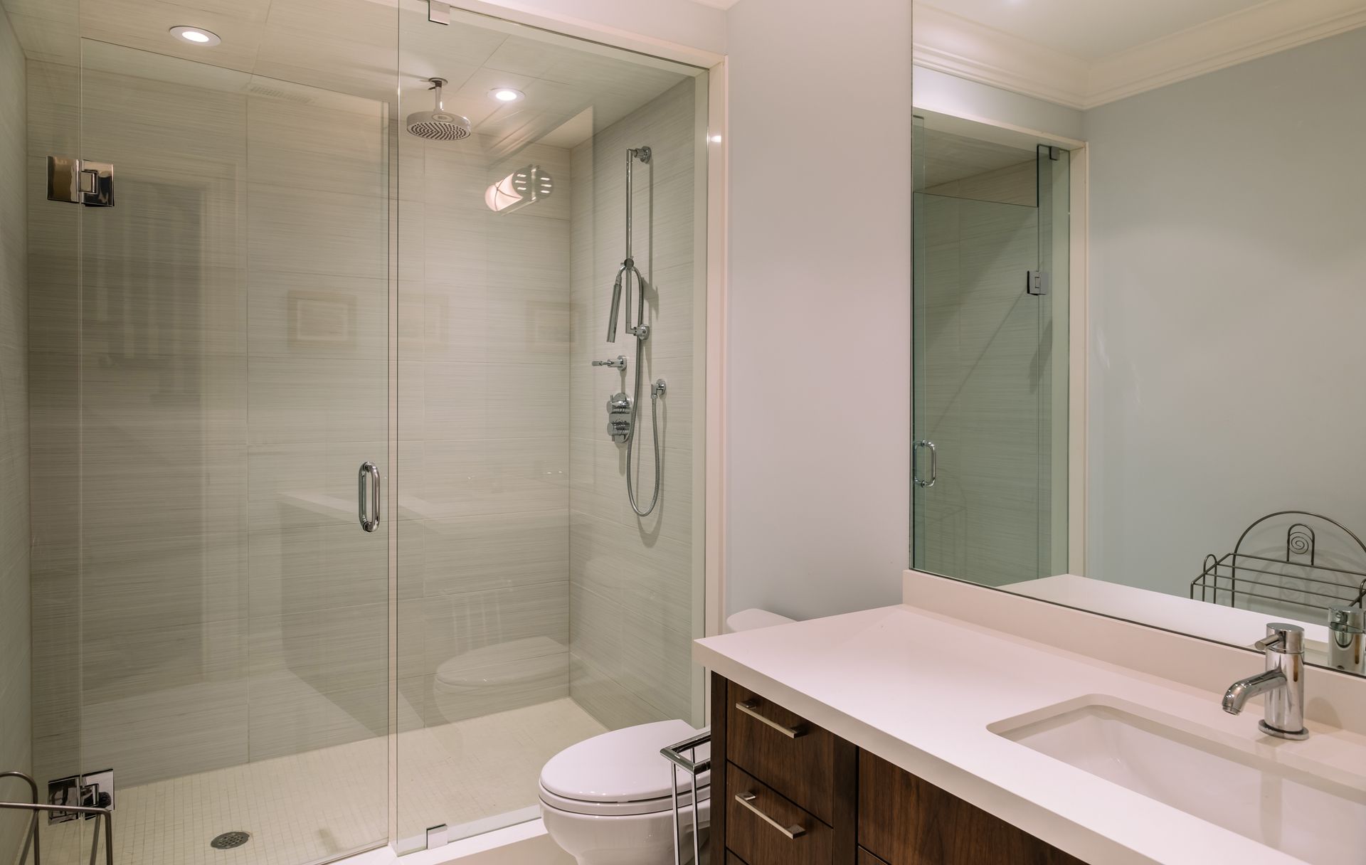 A bathroom with a toilet , sink , shower and mirror.
