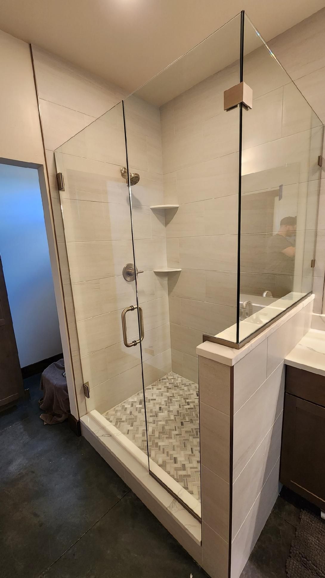 Glass-enclosed shower with white tiled walls, pebble floor, and white shelves.