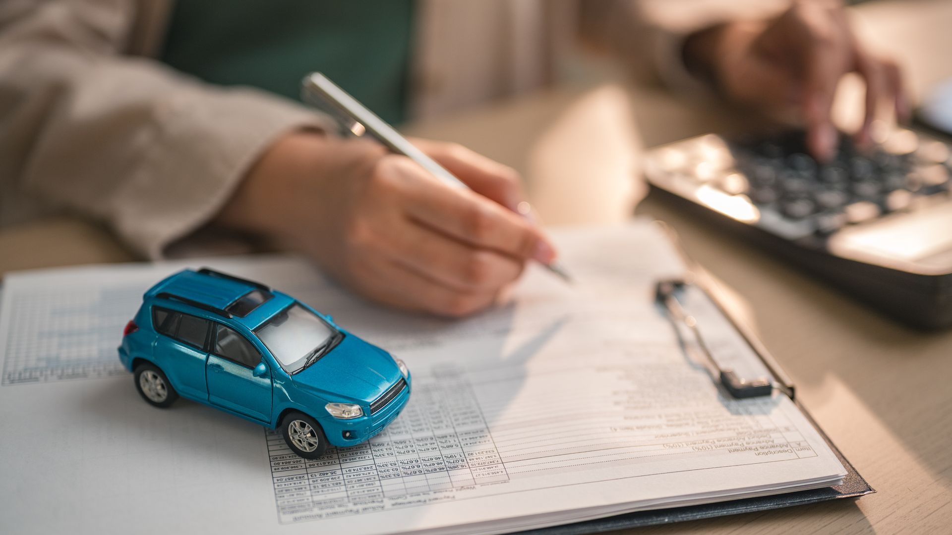 Person completing car insurance paperwork with toy car model and calculator on desk 