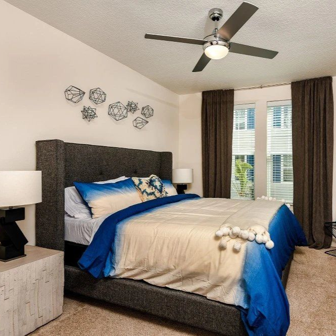 Bedroom with blue and tan bedding, dark wood dresser, a window, and a ceiling fan.