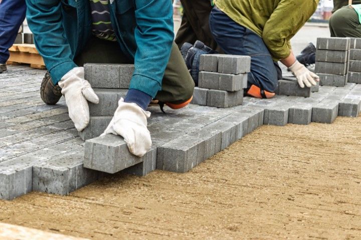 A group of people are laying bricks on a sidewalk.