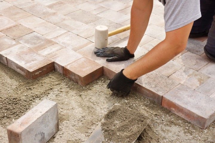 A person is laying bricks on the ground with a hammer.