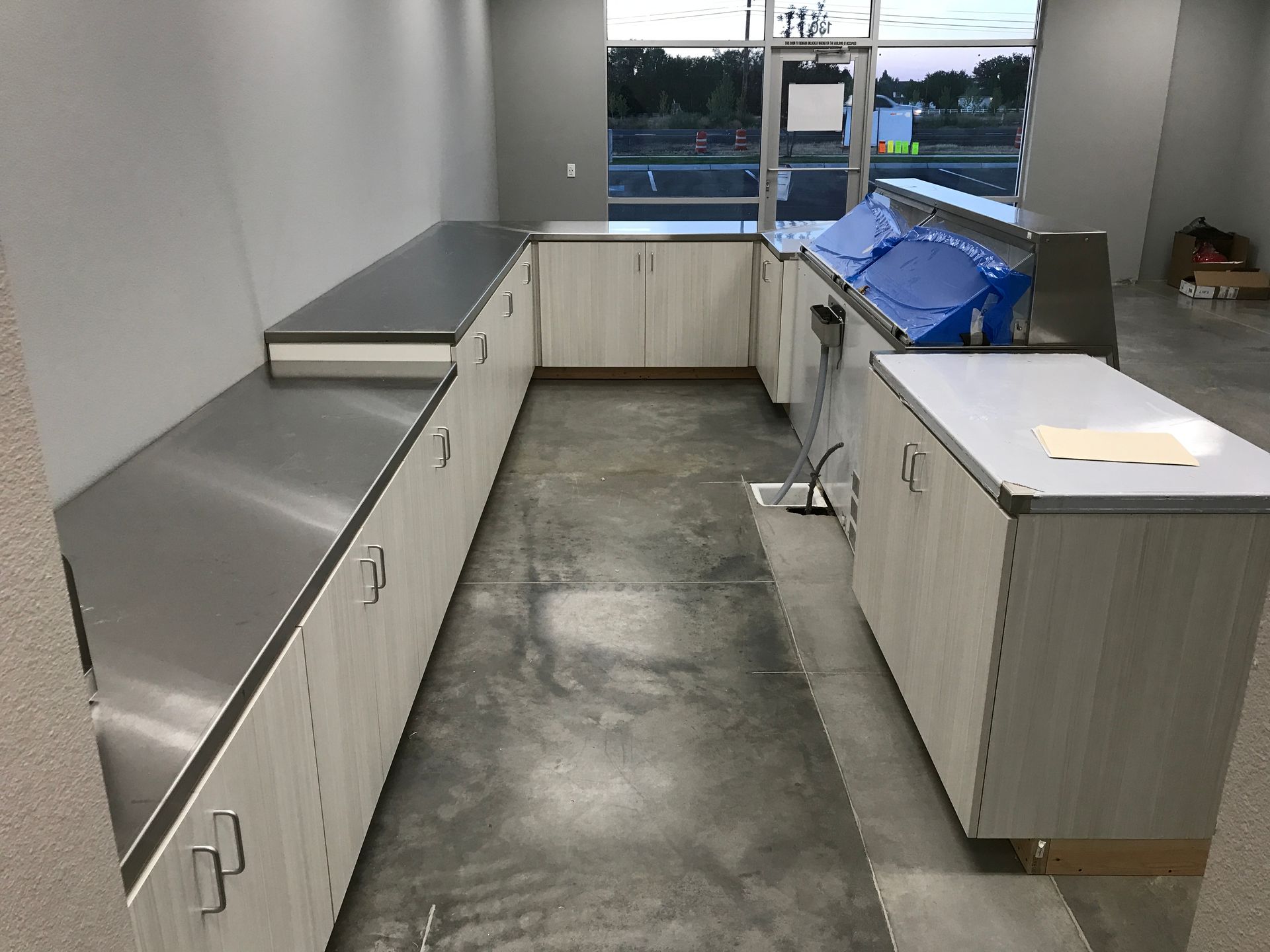 U-shaped room with light wood cabinets and stainless steel countertops. Large window in the background.