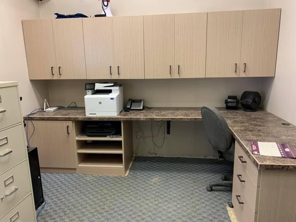 Office workspace with overhead cabinets, desk, printer, phone, filing cabinet, and rolling chair.