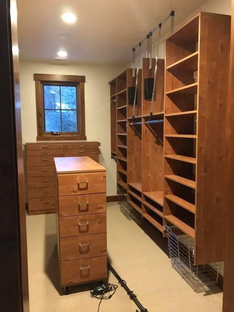 Wooden walk-in closet with shelving, drawers, and a window. Interior shot with light tan walls and flooring.