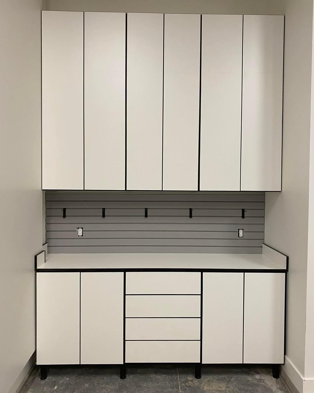 White cabinets with drawers, work surface, gray pegboard, and black hooks on a wall.