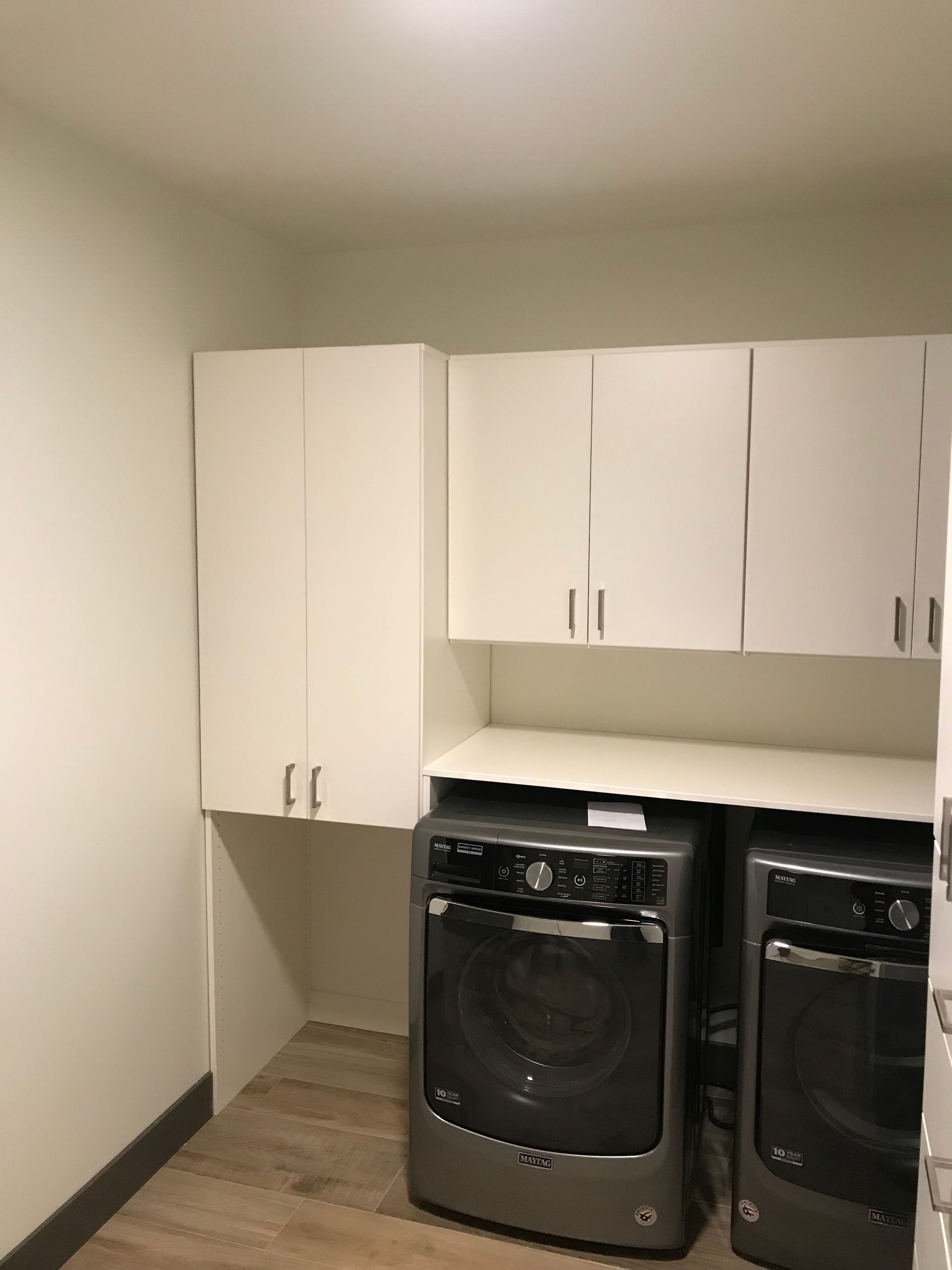Laundry room with white cabinets above a washer and dryer on a wooden floor.
